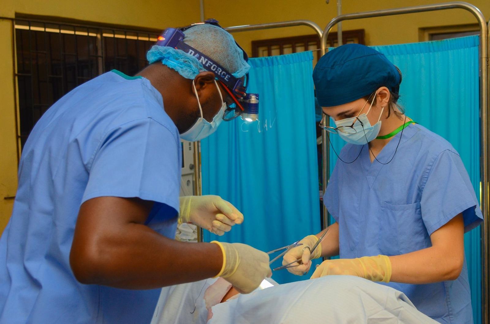 Dr. Adeboye operating beside a young volunteer surgeon