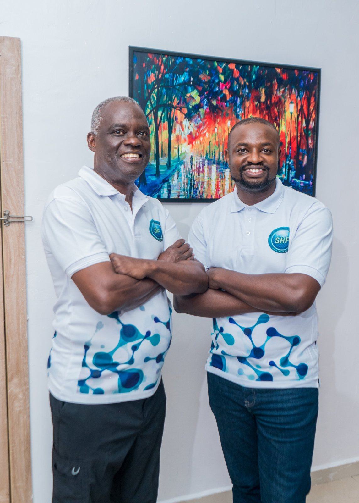 Dr. Adeboye standing with a Shekinah team member, both in SHF shirts, arms crossed and smiling